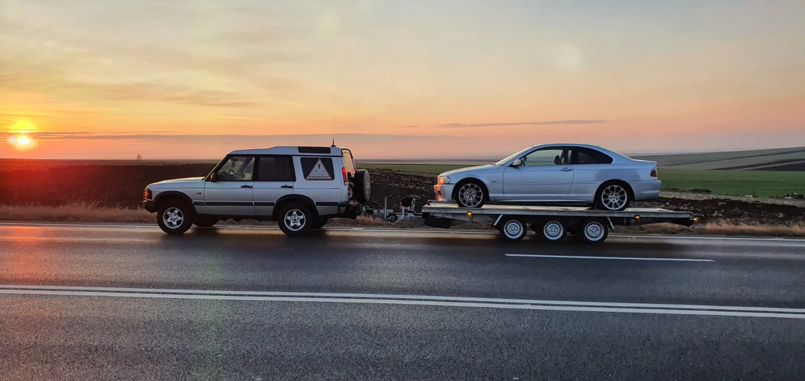 Un BMW pe remorca cu trei axe, la apus.