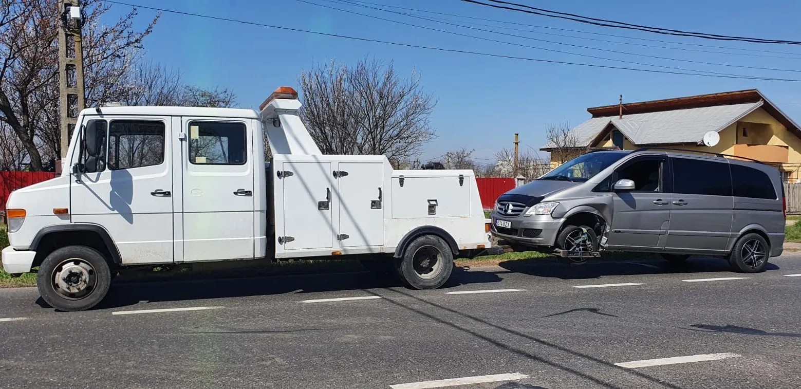 Recuperator auto alb, cu girofar, care tractează un Mercedes Viano ridicat pe furcă de roțile din față