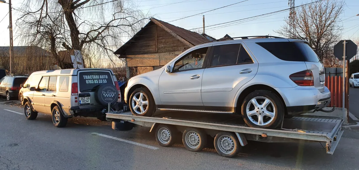 Mercedes ML gri încărcat pe remorca-platformă, tractată de un Land Rover